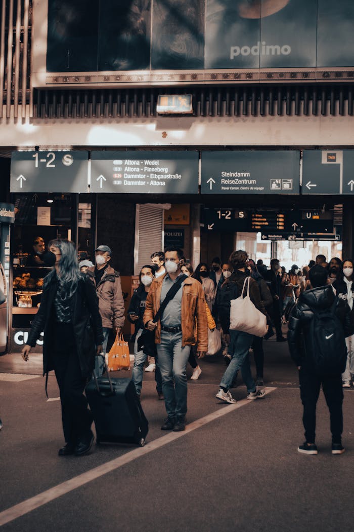 A bustling urban station filled with masked commuters and travelers carrying luggage, embodying modern city life.
